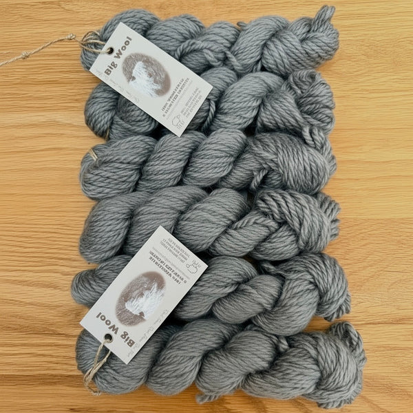 six skeins of gray Wensleydale chunky yarn with tags on a wooden surface